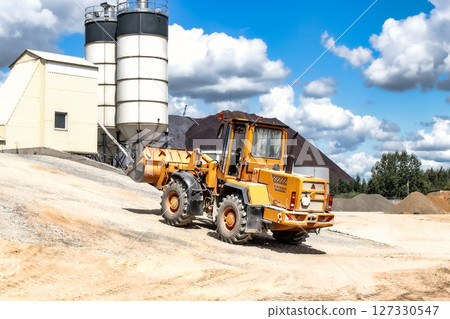A large front loader transports materials in a concrete production plant. Production of concrete. Transportation of bulk materials. Construction equipment. Bulk cargo transportation. A large front loader transports materials in a concrete production plant. Production of concrete. Transportation of bulk materials. Construction equipment. Bulk cargo transportation. 127330547