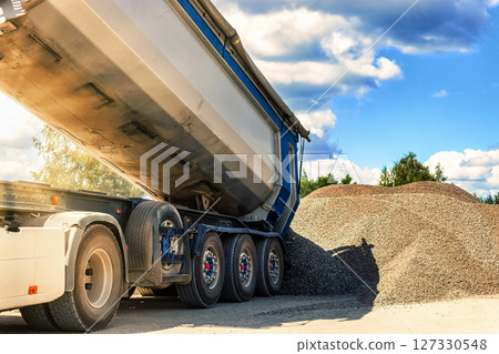A large dump truck unloads rubble or gravel at a construction site. Car tonar for transportation of heavy bulk cargo. Providing the construction site with materials. 127330548