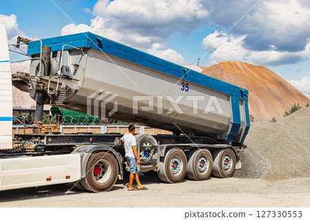 A large dump truck unloads rubble or gravel at a construction site. Car tonar for transportation of heavy bulk cargo. Providing the construction site with materials. 127330553