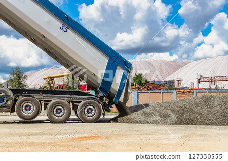 A large dump truck unloads rubble or gravel at a construction site. Car tonar for transportation of heavy bulk cargo. Providing the construction site with materials. 127330555