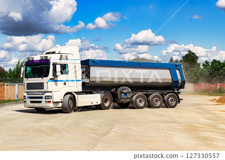 A large dump truck unloads rubble or gravel at a construction site. Car tonar for transportation of heavy bulk cargo. Providing the construction site with materials. 127330557