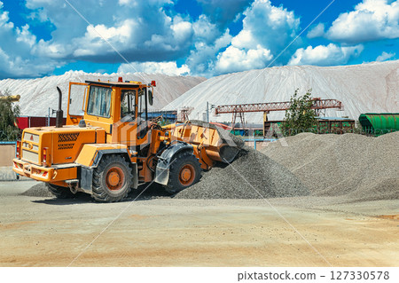 A large front loader transports crushed stone or gravel in a bucket at a construction site or concrete plant. Transportation of bulk materials. Construction equipment. Bulk cargo transportation. 127330578
