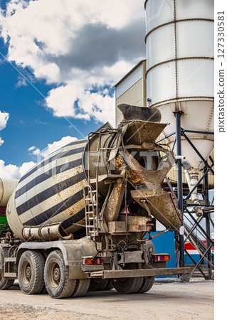 Concrete mixer truck in front of a concrete batching plant, cement factory. Loading concrete mixer truck. Close-up. Delivery of concrete to the construction site. Monolithic concrete works. 127330581