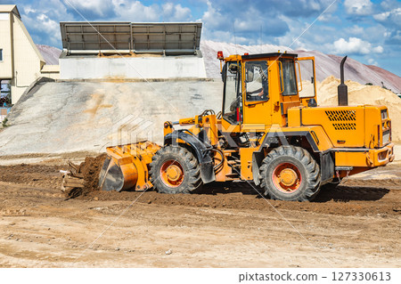A large front loader pours sand into a pile at a construction site. Transportation of bulk materials. Construction equipment. Bulk cargo transportation. Excavation. A large front loader pours sand into a pile at a construction site. Transportation of bulk materials. Construction equipment. Bulk cargo transportation. Excavation. 127330613