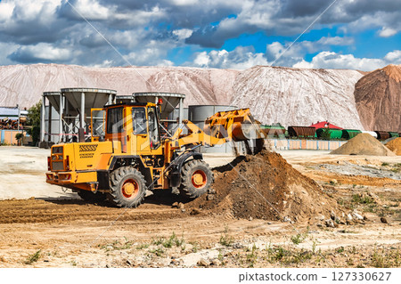 A large front loader pours sand into a pile at a construction site. Transportation of bulk materials. Construction equipment. Bulk cargo transportation. Excavation. 127330627