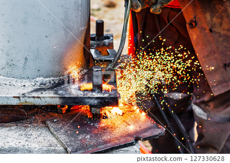 Worker cutting metal plate by Gas Cutting Torch at a construction site. Installation of a metal structure. Close-up. The welder performs the installation of metal structures. Sparks from welding. 127330628