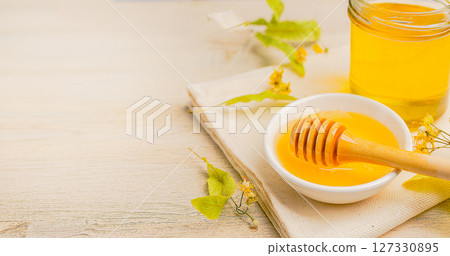 Honey bee in glass jar and bowl with linden flower with honey dipper on wooden background. 127330895