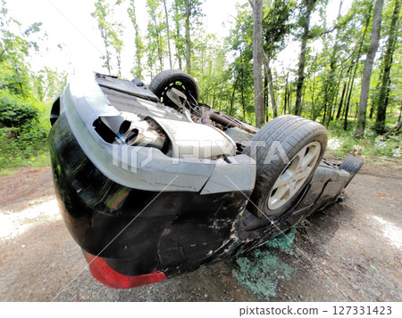 Car is overturned in wooded area, showcasing damage surrounding heavily damaged cars 127331423