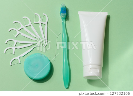 Flat lay composition of various dental hygiene products, including a green toothbrush, white dental floss dispenser, a white dental floss pick, and tube of toothpaste, green background Flat lay composition of various dental hygiene products, including a green toothbrush, white dental floss dispenser, a white dental floss pick, and tube of toothpaste, green background 127332106