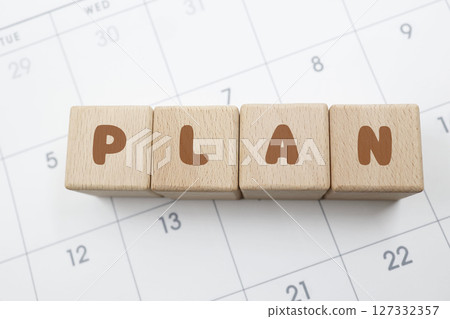 A wooden block with the word PLAN written on it is placed on the calendar. 127332357