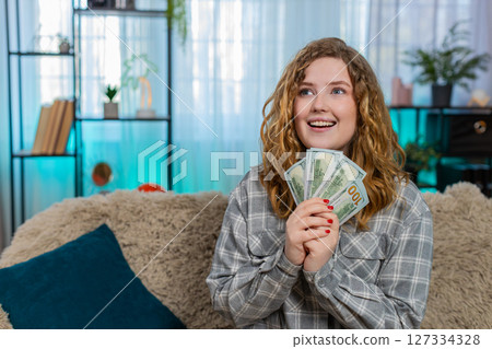 Woman sits on sofa excitedly counting cash dollars celebrating lottery win or unexpected income joy Woman sits on sofa excitedly counting cash dollars celebrating lottery win or unexpected income joy 127334328
