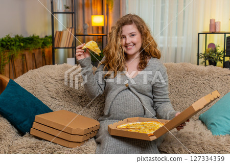 Pregnant woman opening pizza box at home, tasting slice with satisfied smile, enjoying comfort food Pregnant woman opening pizza box at home, tasting slice with satisfied smile, enjoying comfort food 127334359