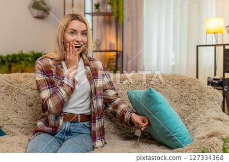 Woman searching under cushions at home for lost keys, feeling relieved after finally finding them 127334368