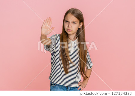 Child girl kid seriously raises hand in stop gesture staring straight into camera with firm look 127334383
