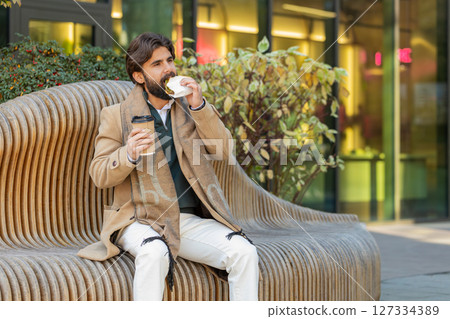 Indian young businessman tourist enjoy lunch break eating sandwich and drinking hot coffee or tea 127334389