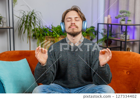 Bearded man listening music, breathes deeply meditating with concentrated thoughts peaceful at home Bearded man listening music, breathes deeply meditating with concentrated thoughts peaceful at home 127334402