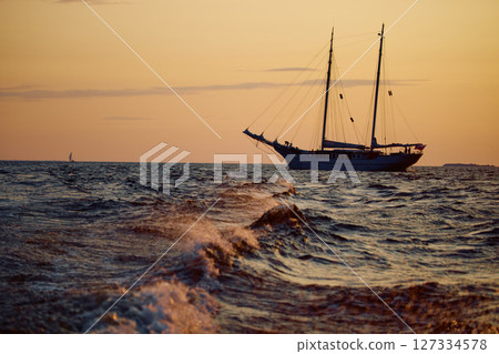 The silhouette of an ancient frigate in the sea at sunset, splashes of waves illuminated by the sun 127334578