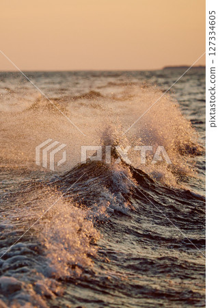 The wave splashes into splashes in the rays of sun at sunset 127334605