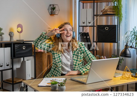 Businesswoman listening music through wireless headphones relaxing taking a break, laptop on table 127334623