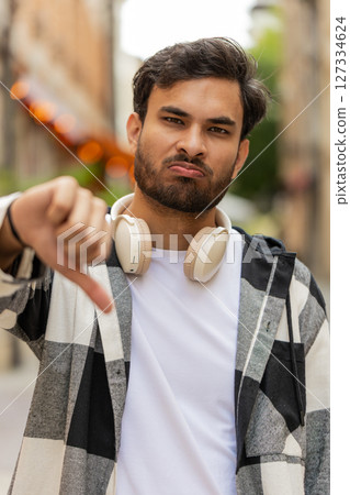 Upset Indian man showing thumb down sign gesture, expressing discontent disapproval in city street 127334624