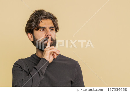 Young Lebanese man presses index finger to lips makes silence gesture over beige studio background 127334668