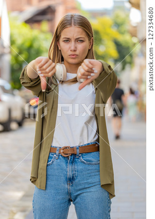Upset young woman showing thumb down sign gesture, expressing discontent disapproval on city street 127334680
