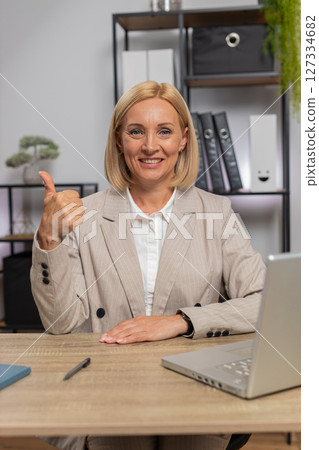 Happy mature Caucasian businesswoman freelancer in formal suit showing thumb up at home office desk Happy mature Caucasian businesswoman freelancer in formal suit showing thumb up at home office desk 127334682