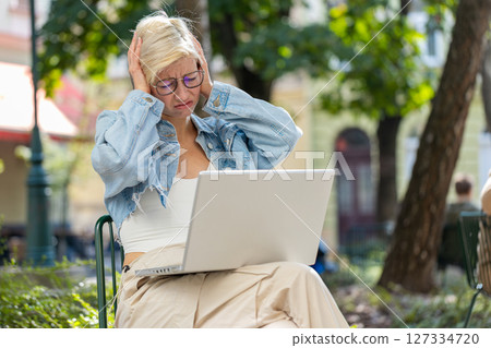 Caucasian young woman using laptop browsing loses lottery results, bad news sitting in city street Caucasian young woman using laptop browsing loses lottery results, bad news sitting in city street 127334720