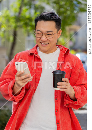Happy Asian man enjoying drinking morning coffee hot drink, relaxing, taking a break on city street Happy Asian man enjoying drinking morning coffee hot drink, relaxing, taking a break on city street 127334752