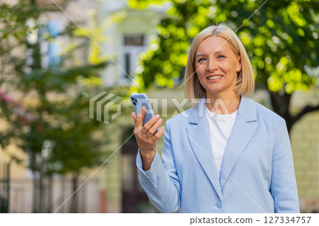 Caucasian mature businesswoman in suit using mobile GPS to find a direction walking on city street 127334757
