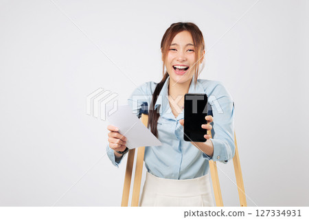 Patient on crutches holds bill paper and phone with blank screen proudly. Crutches symbolize support as she navigates accident payment confidently. insurance isolated studio white background Patient on crutches holds bill paper and phone with blank screen proudly. Crutches symbolize support as she navigates accident payment confidently. insurance isolated studio white background 127334931