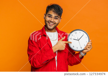 Indian young man showing time hour on wall office clock, ok, thumb up, approve, hurry up, deadline Indian young man showing time hour on wall office clock, ok, thumb up, approve, hurry up, deadline 127334974
