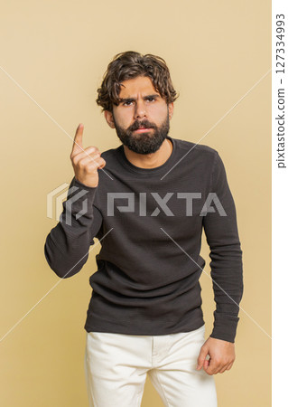 Displeased young Hindu man gesturing hands with irritation and displeasure against beige background 127334993