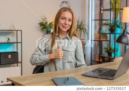 Happy Caucasian woman looking approvingly at camera showing thumbs up sitting at home office table Happy Caucasian woman looking approvingly at camera showing thumbs up sitting at home office table 127335017