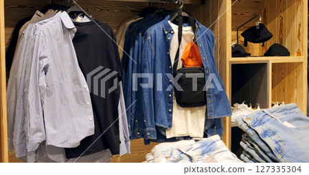 Multiple denim shirts, t shirts, jeans, and accessories are neatly arranged on hangers and shelves in a modern clothing store, creating appealing visual display for customers. Concept fashion clothes 127335304
