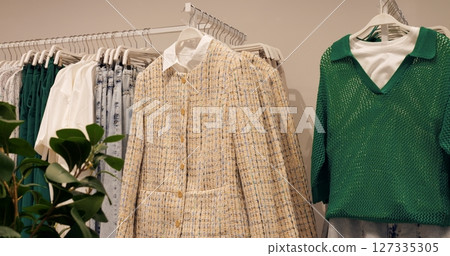 Light yellow tweed jackets and green knitwear are displayed on hangers in a clothing store, offering a glimpse into the latest fashion trends for women. Concept fashion clothes 127335305