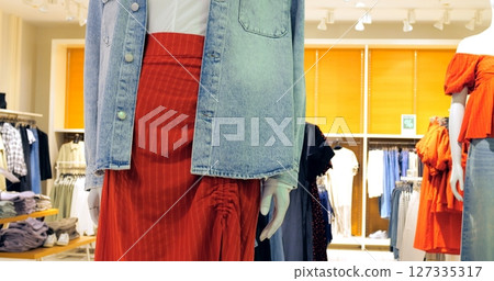 Fashion retail store presenting various clothing items on mannequins, including a stylish denim jacket, white shirt, and a vibrant red skirt combination. Concept fashion clothes 127335317