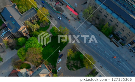 Campus aerial view rotating clockwise, revealing sunlit street with cars driving past green areas, buildings, and trees during spring afternoon. Urban style concept USA 127335366