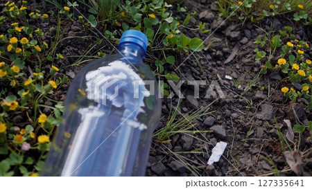 Empty plastic bottle lies on the ground among green grass and yellow flowers, illustrating environmental pollution and the need for responsible waste disposal 127335641