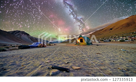 Glowing tent standing on sandy terrain, milky way and vibrant aurora borealis illuminating starry nocturnal landscape 127335913