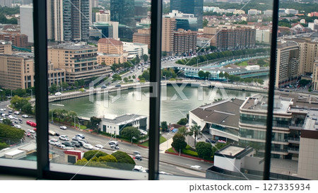 Xiamen urban landscape, bustling traffic passing canal, sleek skyscrapers viewed through glass, cloudy atmosphere highlighting southeastern chinese metropolitan scene 127335934