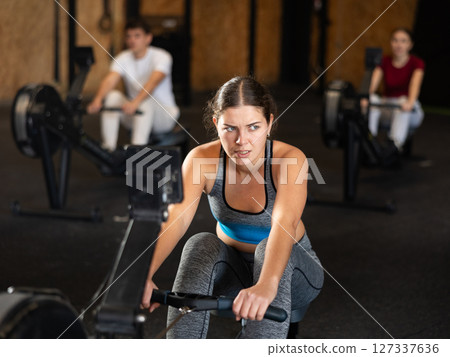 Woman in top exercising on rowing machine 127337636