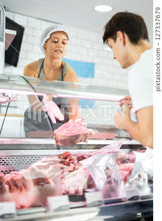Young female seller offers guy to buy fresh beef entrecote boneless meat Young female seller offers guy to buy fresh beef entrecote boneless meat 127337679