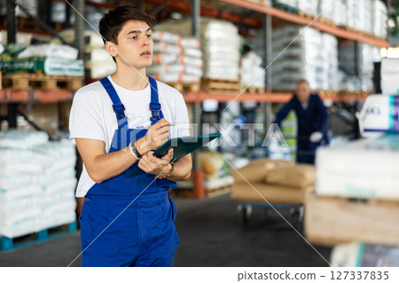 In warehouse of store, guy checks quantity of goods and receipt documents for products In warehouse of store, guy checks quantity of goods and receipt documents for products 127337835