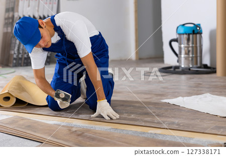 Young builder laying laminate flooring with rubber mallet in repairable room Young builder laying laminate flooring with rubber mallet in repairable room 127338171