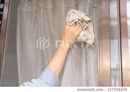 Senior woman wiping the screen door with a rag 127338244