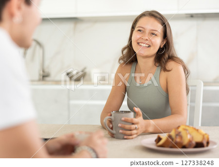 Happy young couple sitting at the kitchen-table and having conversation while drinking tea Happy young couple sitting at the kitchen-table and having conversation while drinking tea 127338248