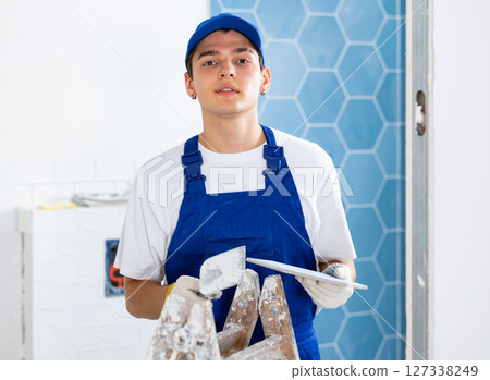 Construction worker in work clothes engaged in wall tiling work during overhauls indoors Construction worker in work clothes engaged in wall tiling work during overhauls indoors 127338249