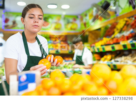 Smiling female seller standing at counter and lay out tangerines in grocery supermarket 127338298