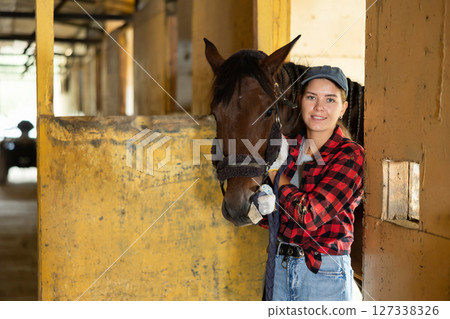 Portrait of smiling woman horse farm worker standing at stable Portrait of smiling woman horse farm worker standing at stable 127338326